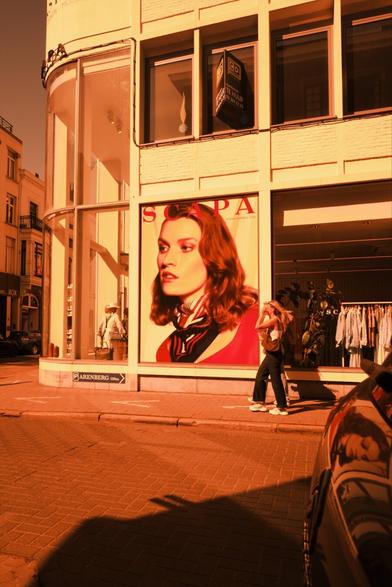 Red scale photo: an advertisement model looking left out of frame, two people approaching from the right with flowing hair