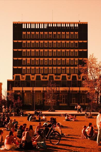Red scale photo: a dark building facade, people on the grass in front of it