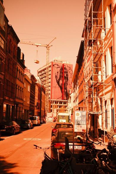 Red scale photo: a streetscape, at its end a tall building with a mural