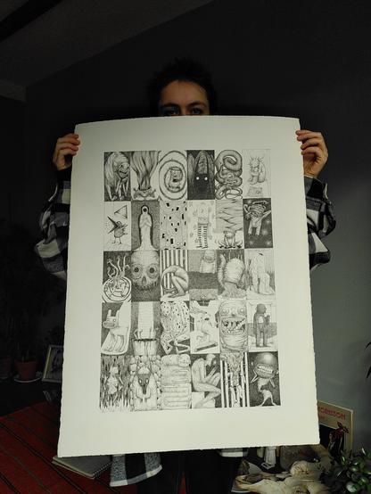 Photo d'ensemble du dessin pour montrer la dimension. On voit le haut de la tête de la personne qui montre le dessin, le dessin recouvre entièrement son buste. La personne porte une chemise à carreaux noirs et blancs.