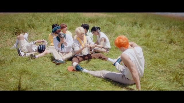 Skz members in the MV for The View. Felix and Bang Chan sit opposite each other with their feet touching. Seungmin's holding an old film camera and pointing it at Bang Chan.