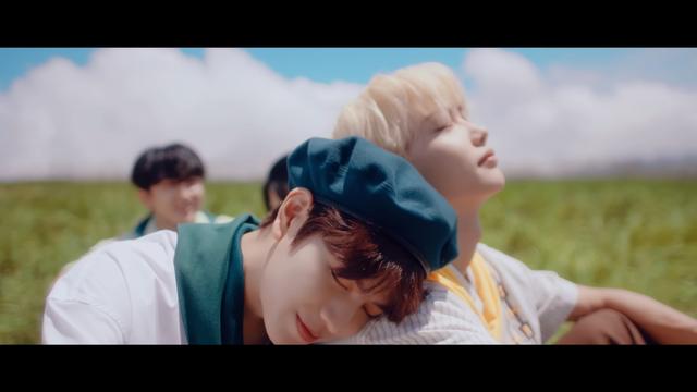 skz members are sitting in a grassy field on a sunny day. Seungmin rests his head on Felix's shoulder. They both have their eyes closed and they look peaceful.