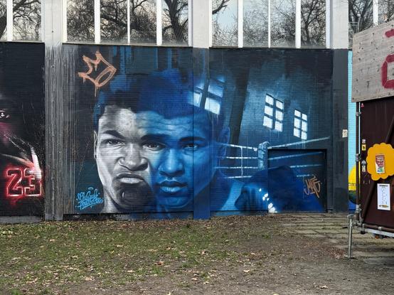 A mural of Muhammad Ali, with a detailed black and white depiction on him on the left, a blue semi-transparent depiction next to it, and a boxing ring to the right.