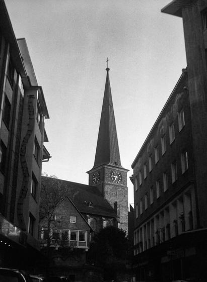 Black an white photo of a church spire seen through an urban street.