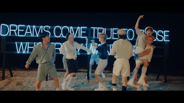 skz members on a beach at night in front of a neon sign. Bang Chan is carrying Han with both arms wrapped around the tops of his thighs