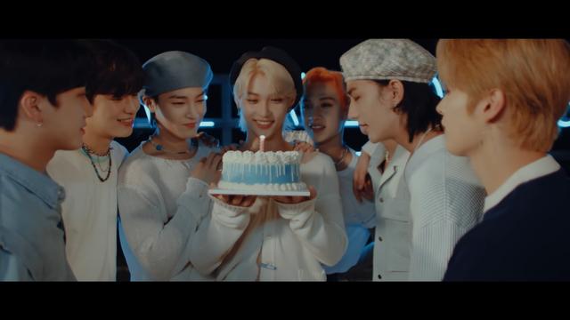 Happy Felix holding the blue cake with the pink candle. Everyone else is gathered around and looking happily at the cake.