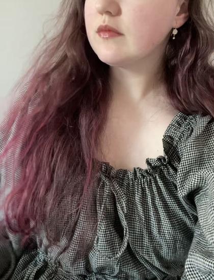 a portrait style photo of Mauni a white person who is wearing a black and beige check linen dress