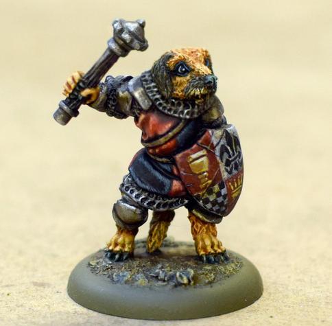 We have an upright anthropomorphic terrier dog 32mm miniature, with brown fur plus a black nose and ears. He's standing upright wearing coloured leather armour and holding a mace with its right paw. In its left paw is a shield painted delicately in quarters: top left a golden chalice on a red background; top right: a blue fleur-de-lys on a white background; bottom right: a gold crown on a red background; and bottom left: a blue and white checkerboard.