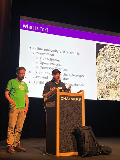 Two persons speaking in front of a lectern speaking about tor.