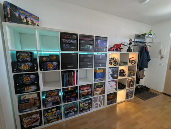 Same two shelves, image taken from the other corner of the room, i.e. from the left of the shelves.
Further back, behind the shelves and to the wall, a wardrobe hangs on the wall. It has a glass plate on top of it, and there's a green Lego Lamborghini model on it.