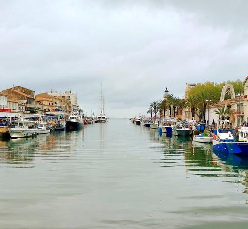 Photo de la sortie du port du Grau du Roi
Au milieu le canal qui s’ouvre vers le monde via la #Méditerranée
De chaque côté des bateaux de pêche 
Il fait gris, le ciel et la mer se confondent à perte de vie