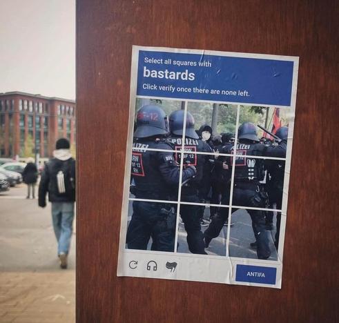 A poster on a wood coloured wall depicting an internet Captcha images typically instructing users to "select all squares" in which in all square are police officers beating street demonstrators (humour)