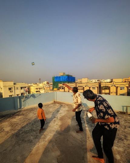 Two adults and one kid flying kite on roof top in India during the dusk