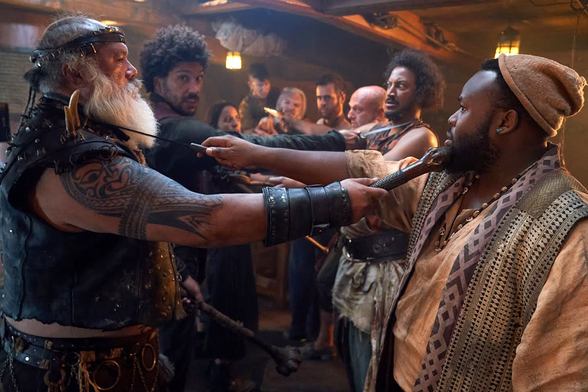 Photo of the same scene, taken from a slightly different angle and without the clapperboard, directly after “action” has been called. The cast are now standing less stiffly and staring at each other with more intensity than before the take started.