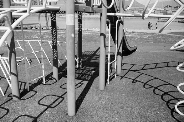 Playground equipment casts playful shadows as people move along the harbour.