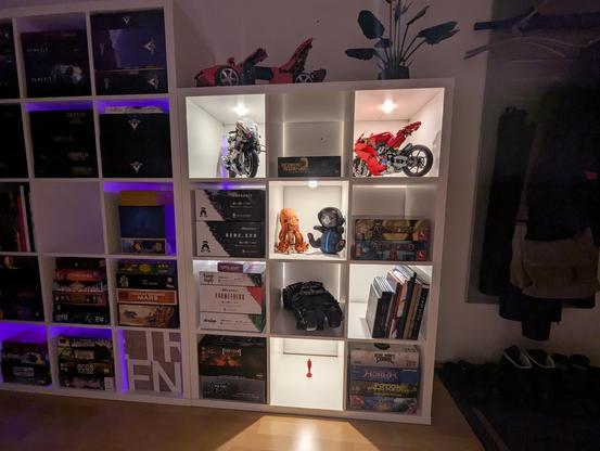 Right Kallax shelf with boardgames, Lego models, plushies. Warm white spotlights make every other compartment bright.