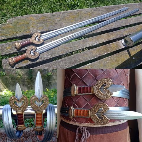 Collage de 3 fotos. La primera muestra dos cinturones que parecen literalmente una de las espadas de las películas de El Señor de los Anillos, guardas de forma redondeada y pomo en oro viejo, y hojas modeladas en plateado, con filo en ambos lados, dos acanaladuras a lo largo de la sección central, con tres pequeños agujeros cerca de la punta; se encuentran estiradas sobre un banco de madera, iluminadas por el sol desde arriba.
La segunda foto es un primer plano de los cinturones, las correas (que son las hojas de las espadas) enrolladas y colgadas de una barra metálica con dos vueltas y con las hebillas echadas (que son las empuñaduras), luz del sol indirecta.
En la tercera, ambos cinturones rodean la cintura de un maniquí que lleva una armadura de cuero ligera, mostrando cómo se ven puestos, y con la luz del sol entrando de lado. Los detalles de las espadas se ven mejor: la guarda muestra dos cabezas de caballo enfrentadas con filigranas de inspiración celta labradas a lo largo de sus cuellos, y el pomo tiene forma trapezoidal, más ancho a la altura del agarre y con más filigranas decorando el frontal
