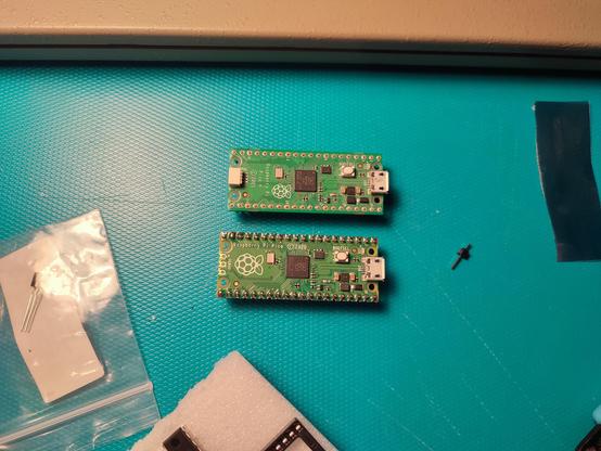 Two RaspberryPi Picos on a plastic mat, a spare Dupont pin near them.