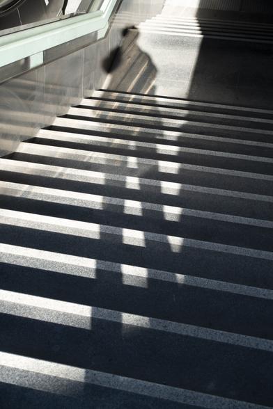 color photograph, portrait format. the shadow of the person photographing on the steps of a subway entrance in the sharp sunlight.