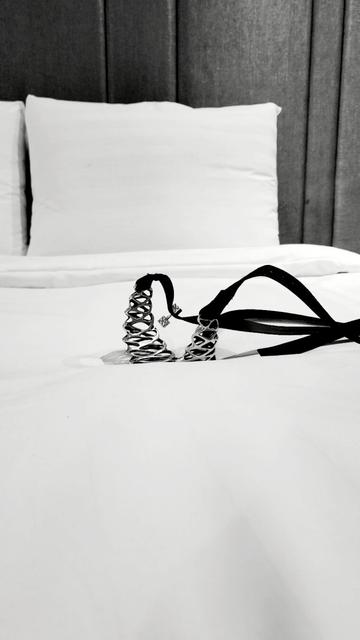 Xover0's solid sterling and black leather choker necklace lies face down on a white bed with a metallic silver padded backboard.