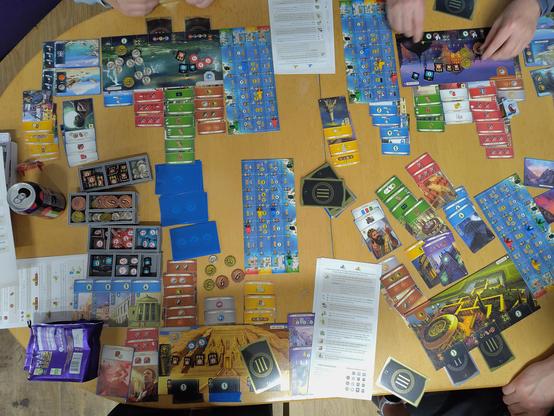 A board game, 7 Wonders, mid-game between four players on a table top.
