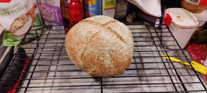 A round loaf of rye bread with an expansion cross cut across the top, sitting on a cooling rack.