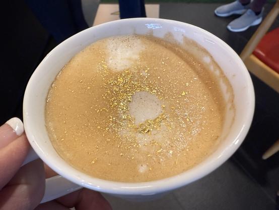 A foamy latte in a white cup with tiny reflective gold flecks