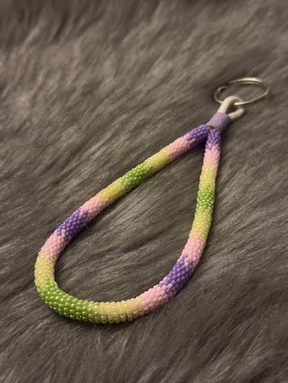 A bead wrapped wristlet keychain in purple, light pink, buttery yellow, and green sitting on a fuzzy blanket