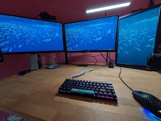 A desk setup. Wooden desktop, 60% keyboard with RGB, three monitors. running KDE desktop on Debian.