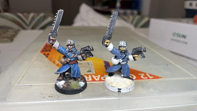 Two identical 90’s era Imperial guard Valhallan Officer models, both painted in blue wearing Russian World War Two style clothing. The one on the left is painted in far crisper detail than the one on the right.