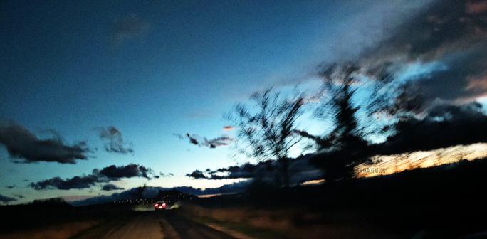 Crépuscule. Route. Les phares arrières d'une voiture. Le ciel encore enflammé et les arbres à contre-jour se mêlent dans les traînées de vitesse.