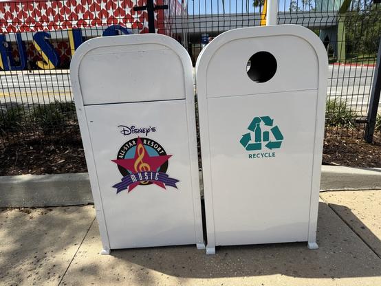 Image of two trash cans at Disney's All-Star Music Resort. The left bin features a colorful design with a musical theme and the resort's branding, while the right bin is marked for recycling with a green recycle symbol.