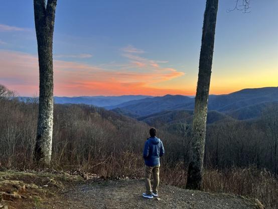 A man stands between two trees at an overlook to view sunset in the Smokies.