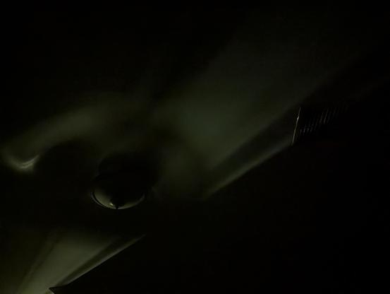 Photo of the ceiling as I lay in bed with the fan on the left and air conditioning vent on the right. A stream of light is across from the bottom left from the bedroom door.