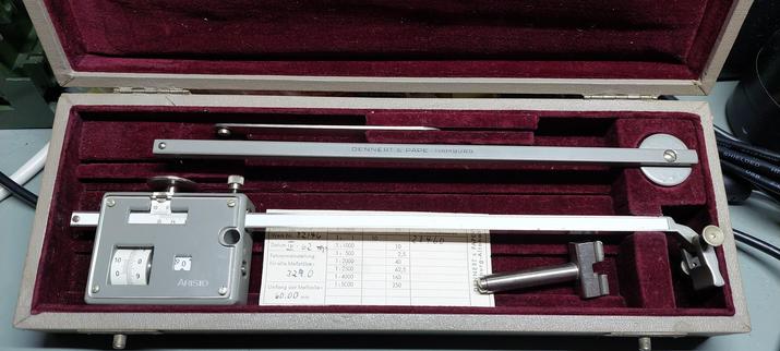 A grey metal tool inside a velvety cushioned box.
The tool has a few scales and wheels on one component. Other pieces may or may not attach to it.