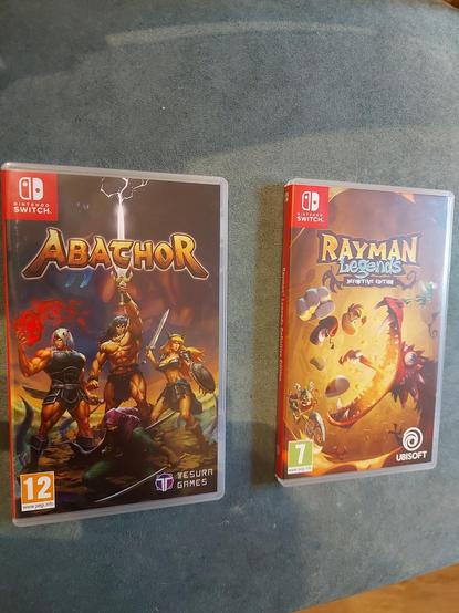 Caja juegos Abathor (aparecen cuatro guerreros, tres de pie, uno agachado) y Rayman Legends (aparece Rayman tirando de lengua a un dragón).