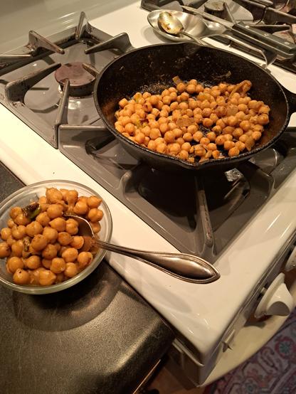 A small skillet of chickpea masala on the stove, and a tiny bowl of it with a spoon. Yum 😋