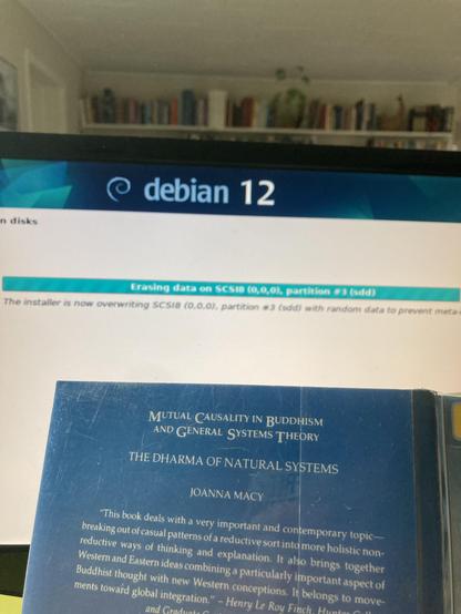 Showing install screen of Debian12 and the back of the book “Mutual Causality in Buddhism and General Systems Theory” by Joanna Macy.
