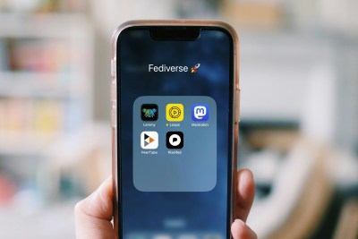 a photo of a hand holding a smartphone - on screen you see the folder "Fediverse" which includes icons for apps like Lemmy, Loops, Mastodon, PeerTube and Pixelfed – aka open source, ethical social media apps that are alternatives to for-profit commercial social platforms by Meta, X, Reddit and Google