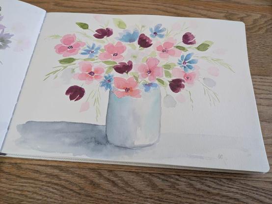 This is a watercolor painting of flowers in a vase.  The flowers are overflowing some leaning down the sides.  The flowers are peach, dark mauve, and cool blue with yellow green greenery. The vase is simple white with shadows.