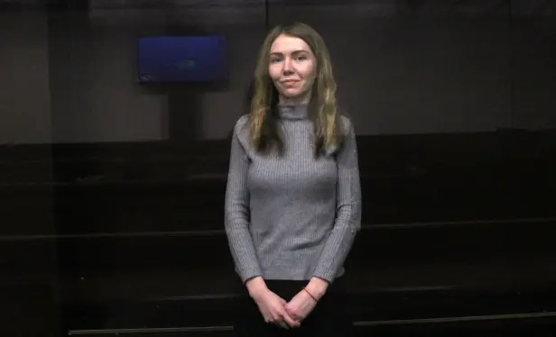 Foto, das Kateryna Korovina zeigt
Eine schmale Frau in einem dünnen grauen Rollkragenpullover, dessen Ärmel vor den Handgelenken enden; auf Schoßhöhe umfasst die rechte Hand die linke, am linken Handgelenk ein rotes Haargummi (mutmaßlich), Haare bis ca. Achselhöhe, leicht gewellt, dunkelblond bis dunkelbraun; Person angedeutet lächelnd, Lippen geschlossen; die Reflexionen in der Scheibe zeigen einen Raum, der im unteren Teil dunkel, im oberen hellbeige gehalten ist, an der Wand (in der Reflexion) ein Flachbildmonitor