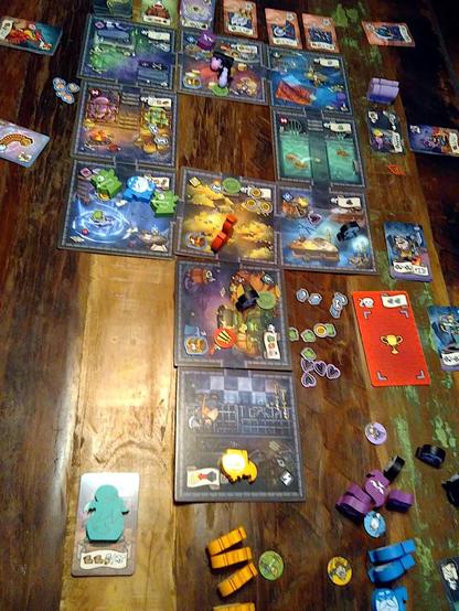 Finale Szene vom Brettspiel „Helden müssen draußen bleiben“, eher von oben fotografiert: Modularer Spielplan auf einem Holztisch, zusammengesetzt aus zehn Räumen, die das Verlies darstellen und mit Durchgängen miteinander verbunden sind. In manchen Räumen stehen oder liegen weiß bzw. schwarz bedruckte, einfarbige Holzfiguren in verschiedenen Formen. Außerhalb des Plans liegen am Rand verschiedene Karten. Alles ist trotz der teils düsteren Räume in recht freundlicher und farbenfroher Comicoptik gezeichnet.