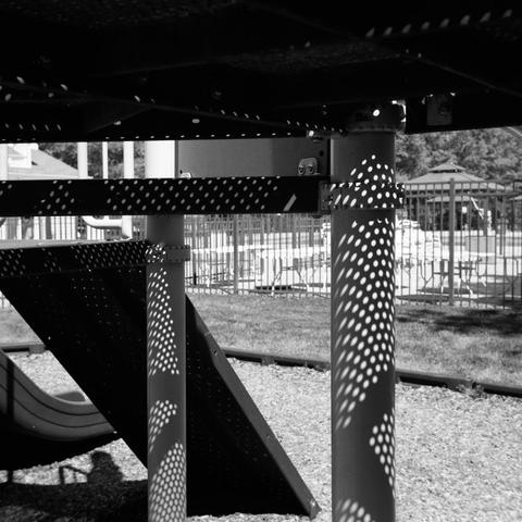 Another view underneath one of the playground platforms, where sunlight is shining through the perforated surface of the platform.