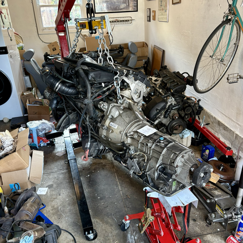The M54B30 inline six-cylinder engine and ZF 5HP19 five-speed automatic transmission that will be going into my 2003 BMW 5-series station wagon hang together from an engine hoist in my garage, with a transmission jack supporting the transmission oil pan.