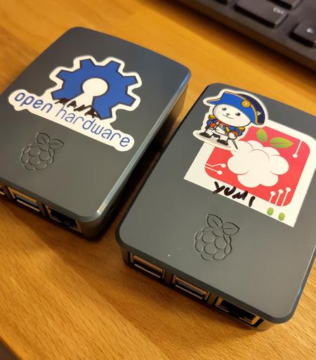 Photo de deux Raspberry Pi 4 dans des boîtiers gris avec des stickers dessus. On peut lire dessus "Yumi" et "Mana" qui sont leurs hostnames.