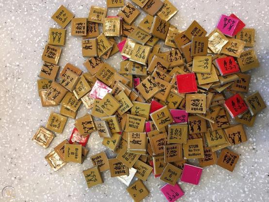A jumbled pile of small, half-inch square wargame counter with teeny tiny writing, numbers, and unit outlines. Most are yellowish brown and a few are red/pink.