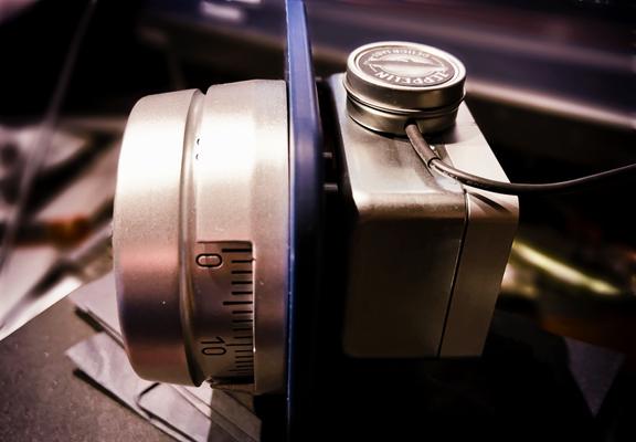 Photo of a chunky-looking brushed metal colored mechanical combination lock mounted on a small blue plastic "demo" stand. There's a contact microphone attached to the top of the lock