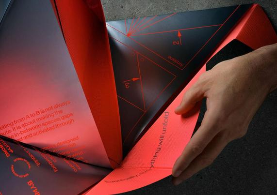 A person folding a geometric, red and black paper design with printed text and numbers. The paper features triangular shapes and a hand interacts with one of the folds on a flat surface.
