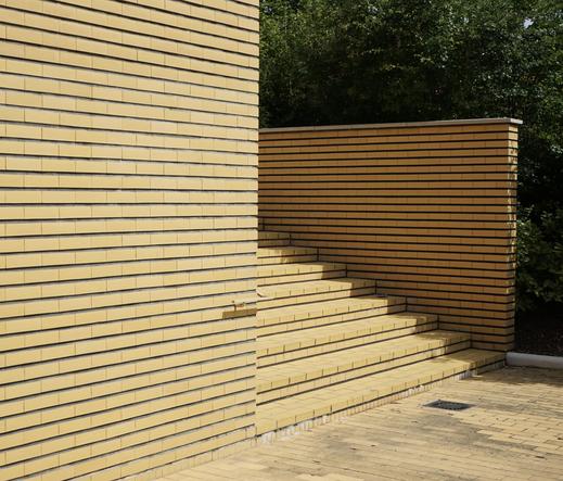 Un escalier en brique jaune encadré de murs en brique jaune avec un peu de végétation au fond.
