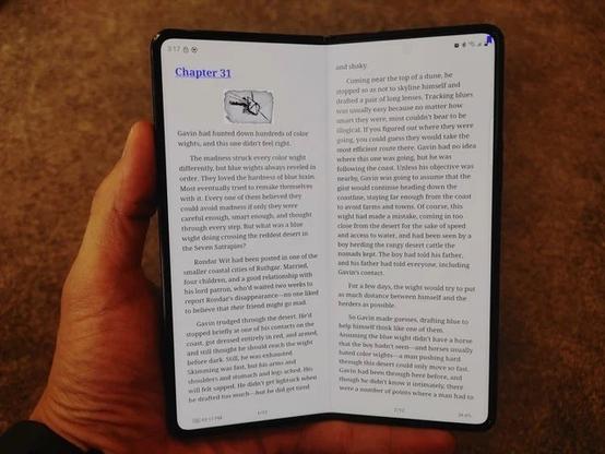 A person is holding a folded smartphone displaying an open ebook. The text on the screen shows "Chapter 31" from a narrative featuring a character named Gavin. The background is a carpeted surface.